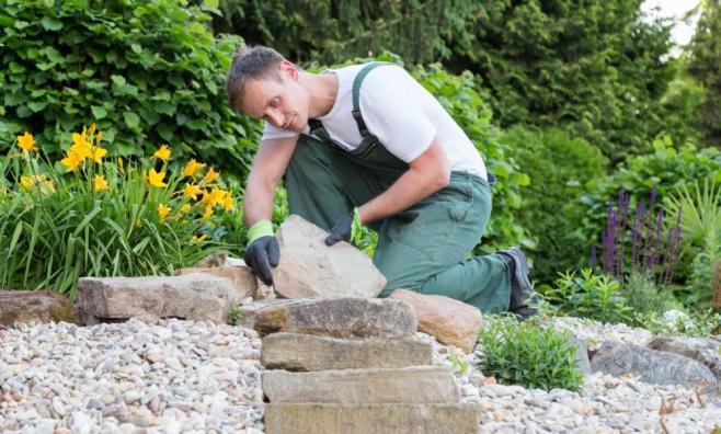 Mann mit grüner Latzhose legt Steinplatten in Garten