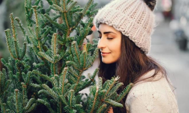 Frau mit heller gestrickter Mütze schnuppert an Weihnachtsbaum